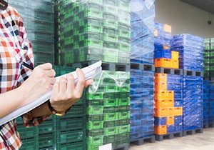 Close-Up shooting hand of quality control with paper sheet checking plastic pallet and empty crates for transportation to goods. Export-Import Logistics system concept.